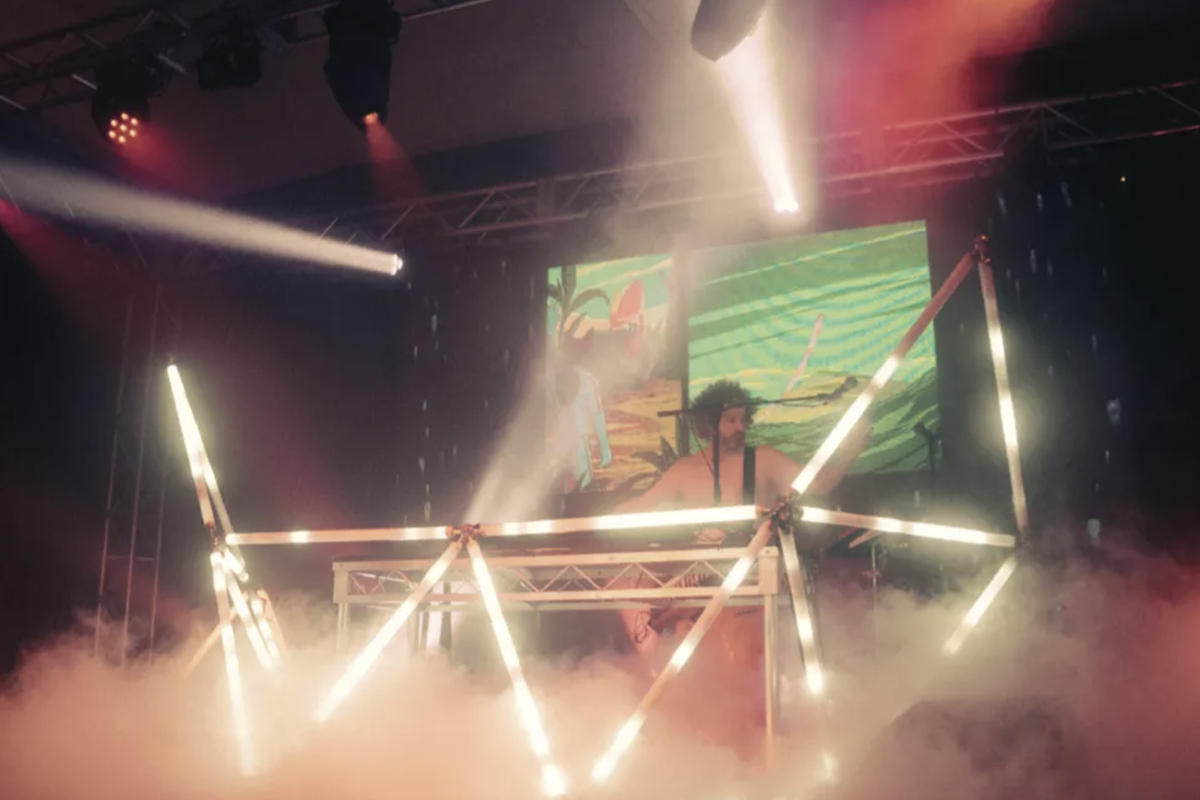 Electronic music producer Luke Million performing live on stage surrounded by heavy smoke, stage lighting, and a custom geometric light-tube setup.